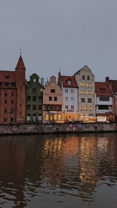 some buildings are next to the water and one is lit up at night with lights on