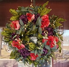 a wreath with red and purple flowers hanging from the side of a window sill