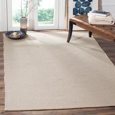 a beige rug with a wooden bench in front of it and a blue vase on the floor