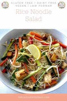 a white bowl filled with rice noodle salad next to lemon wedges and carrots