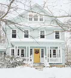 a yellow door sits in front of a white house with snow on the ground and trees