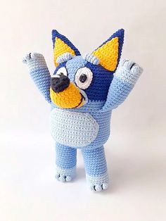 a crocheted blue and yellow stuffed animal with its arms up in the air