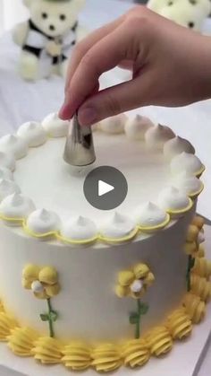 someone is decorating a cake with white frosting and yellow flowers on the bottom