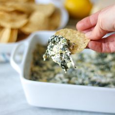 a hand holding up a tortilla chip with spinach and cheese in it