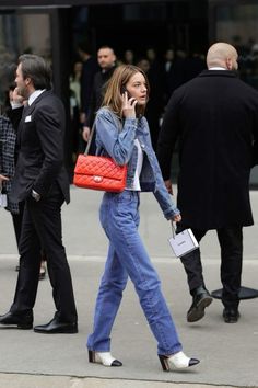 a woman is walking down the street talking on her cell phone and holding a red purse