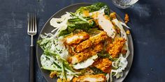 a white plate topped with chicken and salad next to a glass of water on top of a blue table