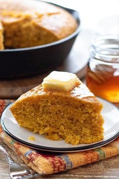 a piece of cake sitting on top of a white plate next to a pan filled with honey