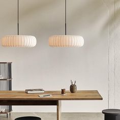 a wooden table sitting under two hanging lights next to a black stool and lamp shade