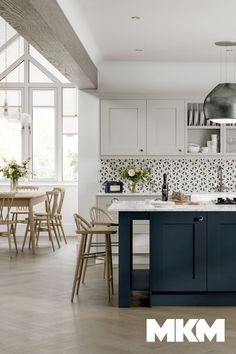 a kitchen with white cabinets and blue island in the center, surrounded by wooden chairs