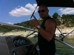 a man on a boat giving the peace sign with his hand as he stands in front of the steering wheel