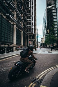 a man riding on the back of a motorcycle down a street next to tall buildings