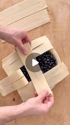 two hands are placing blueberries in a cardboard box on a wooden table with tape