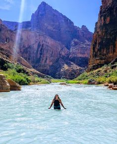 a woman standing in the middle of a river surrounded by mountains