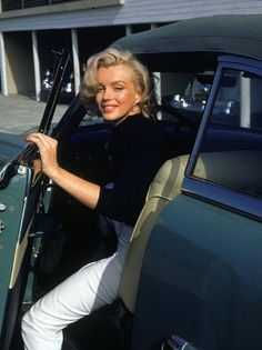 a woman sitting in the driver's seat of a green car with her hand on the door handle