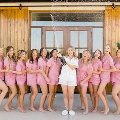 a group of women standing next to each other in front of a wooden building holding champagne bottles