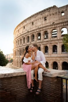 a man and woman sitting on top of a brick wall next to an old building