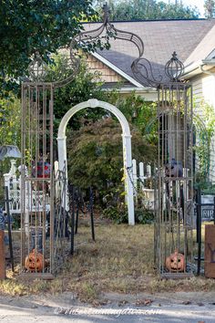 an iron gate with pumpkins in it and other decorations on the front lawn outside