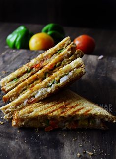 two grilled sandwiches stacked on top of each other next to some tomatoes and peppers