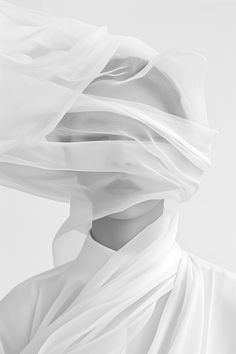 a black and white photo of a woman covered in sheer fabric with her head tilted to the side