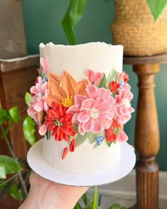 a hand holding a white cake with flowers on it