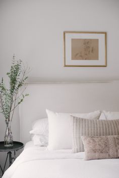 a bed with white linens and pillows in a small room next to a plant