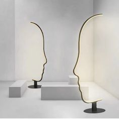 two sculptures with lights on each side of them in a white room, one is shaped like a human head