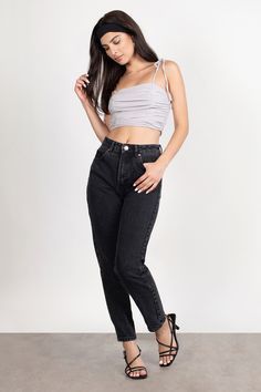 a woman standing in front of a white wall wearing black jeans and a grey tank top