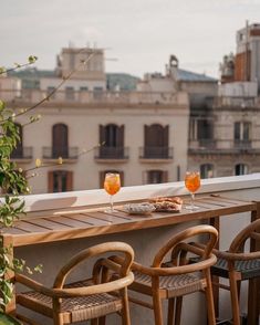 two glasses of orange juice sit on an outdoor table overlooking the cityscape with buildings in the background