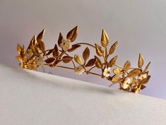 A beautiful simply elegant leaf headband. Slightly raised tiara style. Loops of gold gold delicate golden leaves, tapering from the centre.  Optional hand-carved mother of pearl flowers, which catch the light to give a gentle pearlescent shimmer. Leaves are organically placed (non-symmetrical but balanced). Headband is very light and the ends can be gently bent out to fit a larger head if necessary (I can do this for you before shipping if you prefer. Golden Flower Crown, Greek Gold Leaf Crown, Golden Vine Crown, Gold Elven Crown, Gold Leaf Tiara Wedding, Gold Leaf Crown, Tiara Headpieces, Leaf Crown, Flower Tiara