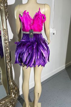 a mannequin wearing a purple and pink feathered dress in front of a mirror