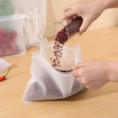 two hands are scooping berries out of a plastic bag on a wooden countertop