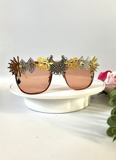 💛Unisex rose gold statement sunglasses by Alexis Exclusive. 💛These unique glasses will add that special touch to your summer / festival / holiday outfits... Be the one and only person in this unique design. 💛The frames are oversized and they have tinted rose gold/orange lenses. All along the top they have been designed in a mixture of funky jewels, embellishments and trinkets. 💛A medium weight design that are comfortable to wear. 💛Great for festivals, weddings, holidays, burning man or everyday wear to add some glam to your outfits.  💛Light UV protection. 💛Exclusive design made by myself, you won't see any others like these anywhere else. 💛All my glasses come in a black branded pouch to keep them safe, please also handle with care. 💛Checkout the full collection of Sunnies here : Spring Party Sunglasses With Metal Frame, Chic Metal Sunglasses For Party, Elegant Gold Shield Sunglasses For Summer, Party Sunglasses With Metal Frame And Glass, Glamorous Gold Sunglasses For Party, Glamorous Gold Party Sunglasses, Pink Shield Sunglasses For Party, Gold Mirrored Shield Sunglasses For Parties, Trendy Metal Sunglasses For Festivals