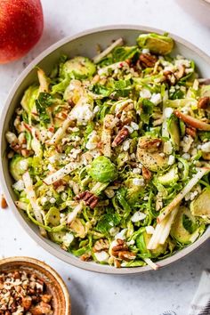 a bowl filled with lettuce and nuts next to an apple on the side