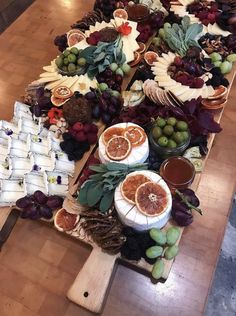 an assortment of fruits and cheeses laid out on a long wooden table with utensils