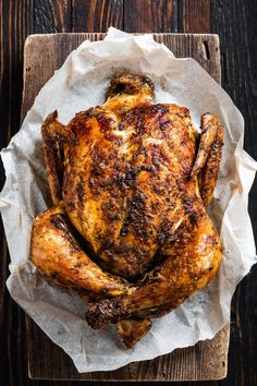 a roasted chicken on a wooden board with some wax paper and seasoning in it