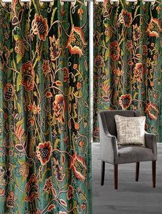 a chair sitting next to a window covered in green and orange floral curtain drapes