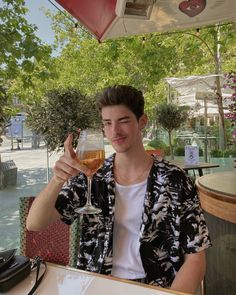 a man sitting at an outdoor table with a glass of wine in front of him