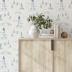 a white vase sitting on top of a wooden cabinet next to a wallpaper covered with boats