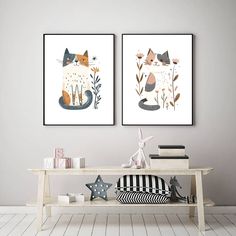 two framed art prints on the wall above a table with books and toys in front of it