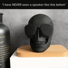 a black skull with sunglasses on top of a wooden table next to a bottle that says, i have never seen a speaker like this before