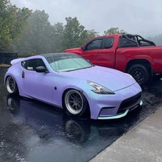 two cars are parked in the parking lot on a rainy day, one is purple and the other is red