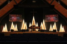 a church stage decorated for christmas with lighted trees and welcome signs on the side wall