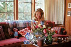 a woman sitting on top of a couch next to a table with flowers in it