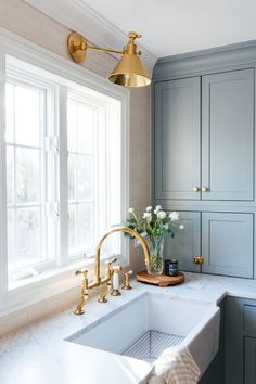 a kitchen sink with gold faucet and marble counter top next to a window