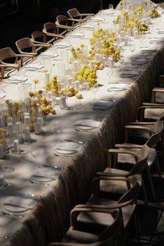 a long table is set up with many glasses and yellow flowers in vases on it