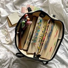 an open suitcase filled with lots of books on top of a white sheet covered bed