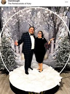 a man and woman posing for a photo in front of a christmas backdrop with trees