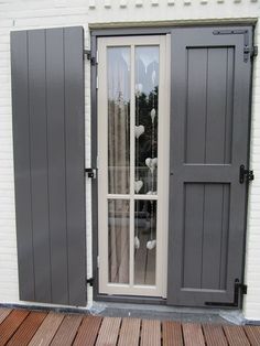 an open door with grey shutters on the outside and wooden flooring in front