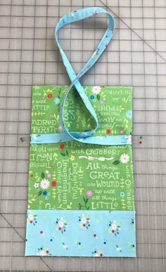 a green and blue bag sitting on top of a piece of fabric next to a ruler