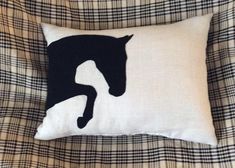 a black and white pillow with a horse silhouette on it sitting on a plaid couch